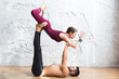 © uv_group - Couple practicing acro yoga poses in studio or gym. Men and woman, pair and acroyoga flexibility class workout on white brick wall background