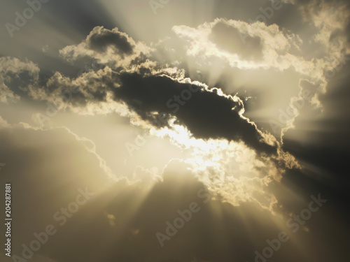 Fotografía Glowing sun hide and seek behind in clods on a cloudy day, camera facing directl
