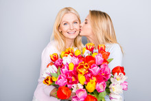 Family With One Parent, Stylish Trendy Cheerful Daughter Congratulate Her Charming Mother  Presenting Big Bouquet Of Colorful Tulips Kissing In Cheek Isolated On Grey Background