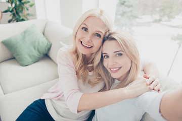 Wall Mural - Self portrait of pretty charming attractive mother and daughter bonding shooting selfie on front camera sitting on couch in living room enjoying free time indoor in comfortable cozy atmosphere