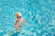 © Елена Нестерова - Cute little baby with sunglasses splashing happily in the pool with clear blue water in the summer. Top view. Copy space.