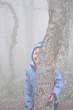 © vitaliiaberestok - Laughing boy hides behind a tree in a misty forest