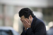 © Erickson Stock - Young adult businessman with his head in his hands outside a building.