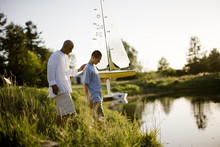 Father And Son Standing Next To Pond With Model Boat
