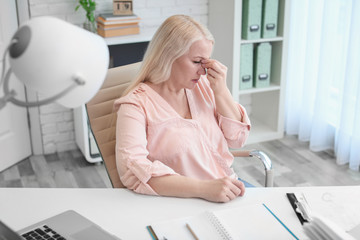 Wall Mural - Mature woman suffering from headache while sitting at table in office