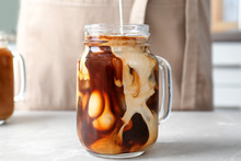 Pouring Milk Into Mason Jar With Cold Brew Coffee On Table