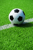 Fototapeta Sport - Klassischer Fussball schwarz weiss auf der Linie mit grünem Kunstrasen in der Sonne im Sommer