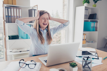 Portrait of stressed, crying, stylish, worried woman in shirt touching her head with two arms, sitting in work place, station at desktop, having close eyes