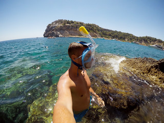 Wall Mural - Partly blurred image because of drops of water. Young male explorer in adventure ready for snorkeling. Selfie shot at summer day at rock in the middle of the sea.