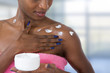 beautiful black skin woman taking care of her body applying moisturizing cream on shoulder