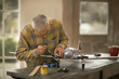 © Erickson Stock - Senior man repairing the propeller of a toy airplane on a workbench in his garage.
