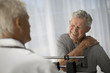 © Erickson Stock - Mature man grips his shoulder in pain while attending a medical examination.