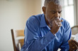 © Erickson Stock - Sick man looks at pill bottle whilst coughing