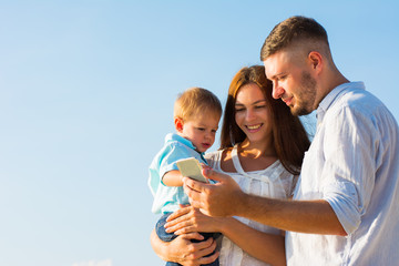 Happy Family are look at mobile phone and hug on the beach While relaxing on weekends with blur sea background in travel and holiday concept.