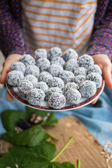 Woman hands holding sweet vegan coconut balls with chocolate, dates, coconut oil, bananas. Indian traditional dessert. Energy bars. Raw vegetarian healthy food