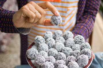 Wall Mural - Woman hands holding sweet vegan coconut balls with chocolate, dates, coconut oil, bananas. Indian traditional dessert. Energy bars. Raw vegetarian healthy food