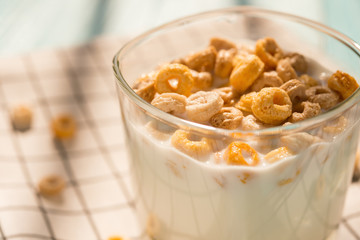 Wall Mural - side view cup of milk with cereal rings in a sunny morning as healthy breakfast close up