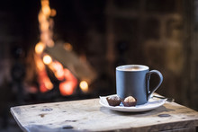 Close Up Of Mug With Hot Drink On Wooden Table In Front Of Fireplace.