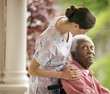© Erickson Stock - Senior man being comforted by a female nurse while sitting in a wheelchair on a porch.
