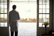 © Erickson Stock - Male doctor standing at doorway,  looking out over courtyard.