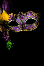 A Purple Mardi Gras Or Venitian Mask With Feathers And Flowers On A Black Background With Copy Space