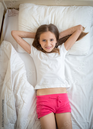 Portrait Of Beautiful Smiling Girl In Pajamas Lying On Bed And Looking 