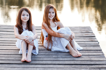 Wall Mural - Beautiful girls friends with long brunette hair ans blue eyes having fun on the pier with beautiful wiev near the water at the sunset