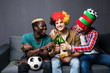 © F8  \ Suport Ukraine - Three fans friends men watching football game, screaming and shouting, drinking beer and eating snaks sitting at couch at home.