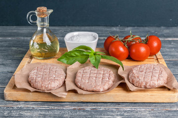 Chicken burgers cutlets on a wooden board with cherry tomatoes and spices