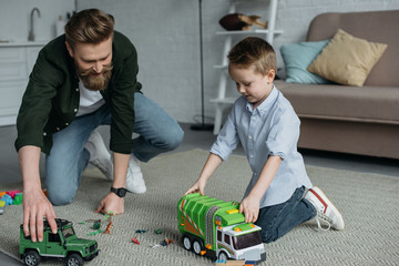 father and little son playing with toy cars together on floor at home