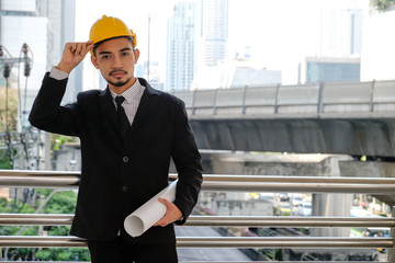 Portrait of Asian supervisor engineer with blueprints, Business man with yellow hard hat standing confidently.concept of work office, security consultant, job control, development and business process