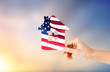 patriotism, home and citizenship concept - hand holding paper house in colors of american flag over evening sky background