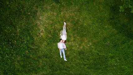 Wall Mural - Young beautiful couple girl and her boyfriend lie on grass opposite, hugging and smiling. Top view