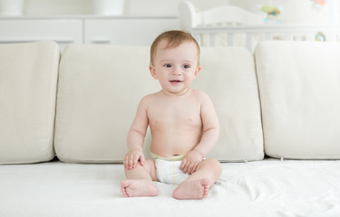 Wall Mural - Cute smiling baby boy in diapers sitting on sofa at bedroom