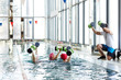 © pressmaster - Three women in water and their trainer in front exercising with barbells during workout at leisure center