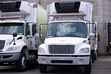 Middle size semi trucks with box trailer and refrigerator unit for local food delivery standing in warehouse dock for loading