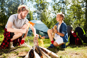 Wall Mural - Boy scout helping his father with preparing firewood for campfire on summer weekend