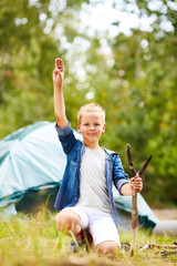 Wall Mural - Little boyscout showing gesture of three fingers put together and looking at you in natural environment