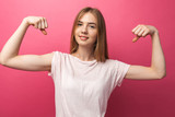 Portrait of cheerful young girl bending biceps isolated on pink background, cute and attractive,
