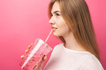 Wall Mural - Portrait of beautiful young woman drinking fizzy drink from a bottle with a straw and looking at camera isolated on a pink background, is the text