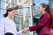 © salomonus_ - Handshake of two young girls against the background of a multi-storey office building. Make a deal. Friendly relations. Office staff