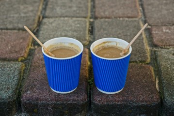 two blue paper glasses with coffee on the sidewalk