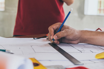 Concept architects,engineer holding pen pointing equipment architects On the desk with a blueprint in the office, Vintage, Sunset light.Selective Focus