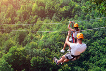 Zipline Is An Exciting Adventure Activity. Man And Woman Hanging On A Rope-way. Tourists Ride On The Zipline Through The Canyon Of The Tara River Montenegro. Couple In Helmets Is Riding On A Cable Car