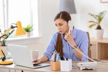 Wall Mural - Young woman talking on phone at workplace