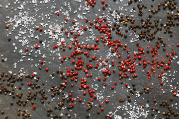 Rock sea salt  scattered with brown and pink peppercorns on slate background