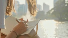 Young Woman Sitting On The Bench In Park And Writing In Diary, Close-up