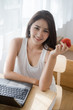 © fufupix - Happy casual beautiful woman hold red apple and working on a laptop sitting in the house.