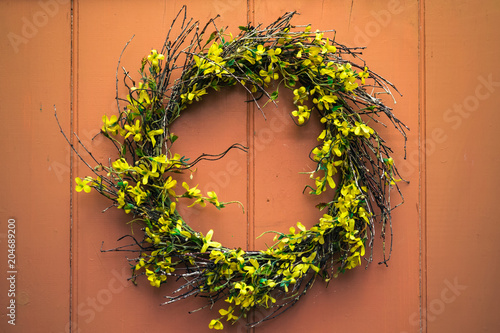Fotografía A yellow forsythia wreath hangs on an old wooden door, with dappled sun and shade playing across its surface