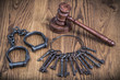 Wooden gavel, vintage handcuffs and antique old door keys on the oak textured table background. Symbols of justice conceptual still life. Retro style filtered photo